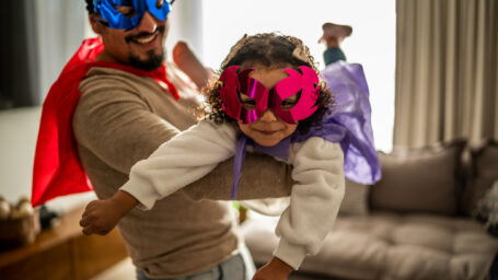 Portrait of father and daughter playing superhero in the living room at home